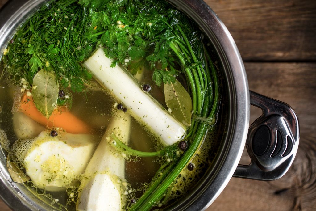 Chicken broth with vegetables in a metal casserole on dark wooden table.